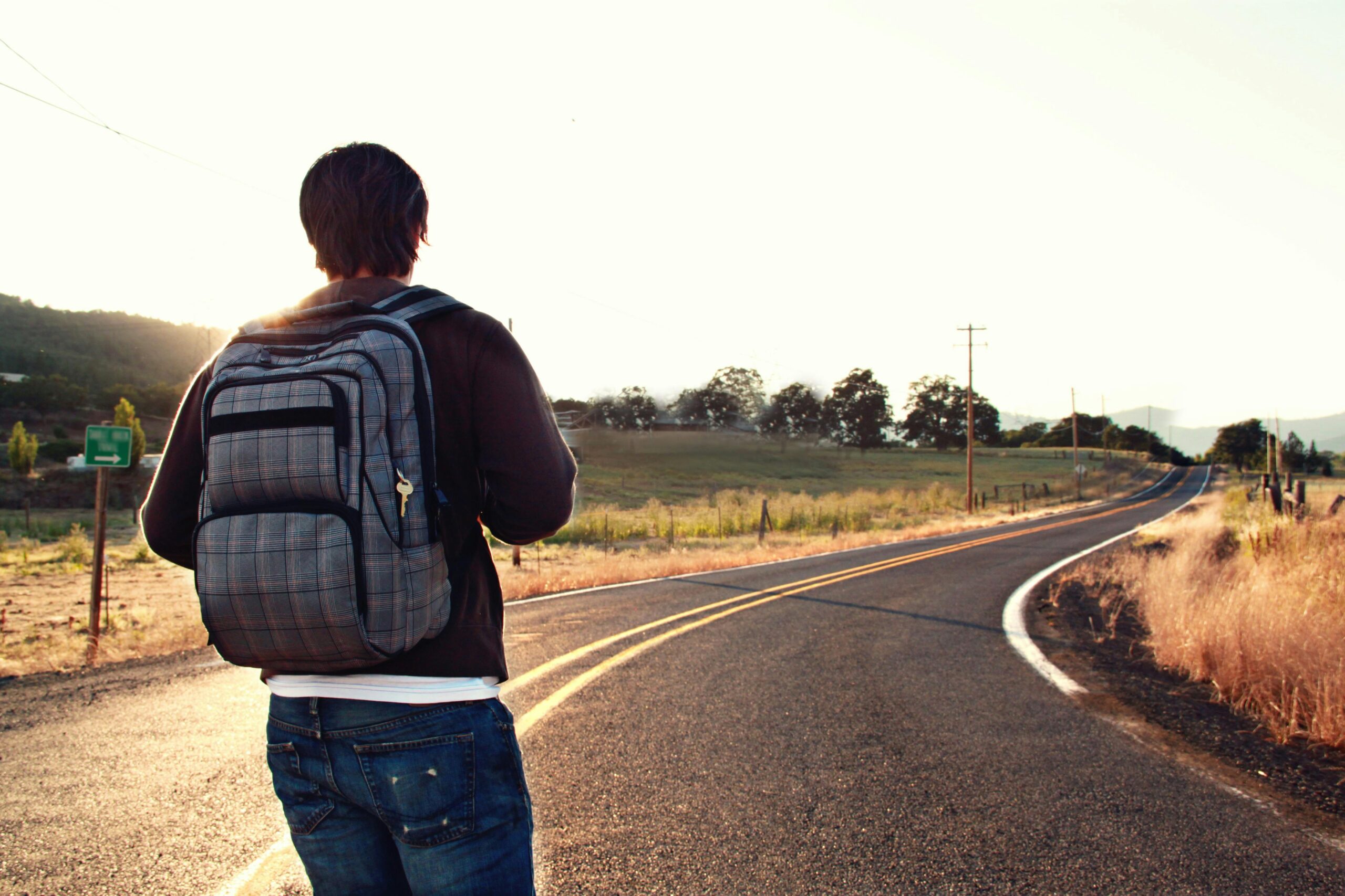 A traveler with a backpack walks on a winding road in the countryside during sunset, symbolizing adventure and freedom.