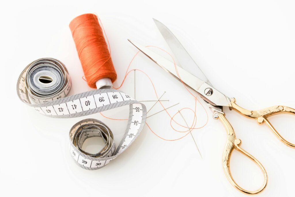 Photo of sewing essentials: scissors, thread, needles, and tape measure on a white background.